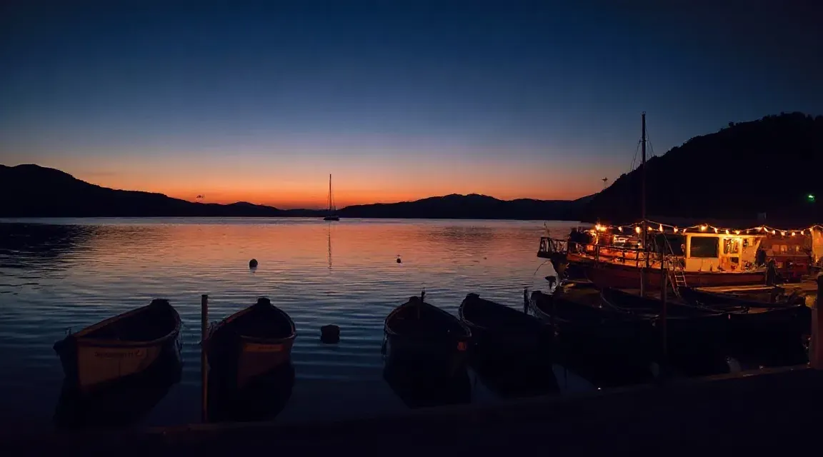 夕焼けの空の下、暗い水面に浮かぶ小舟のシルエット
